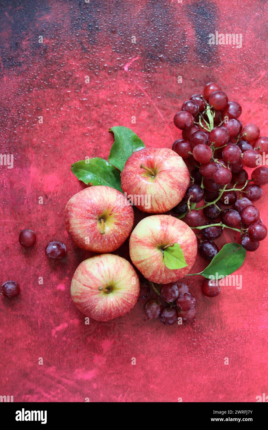 Stillleben im Herbst mit Reifen Äpfeln und Trauben auf einem rot strukturierten Hintergrund mit Platz für Text. Draufsicht. Stockfoto