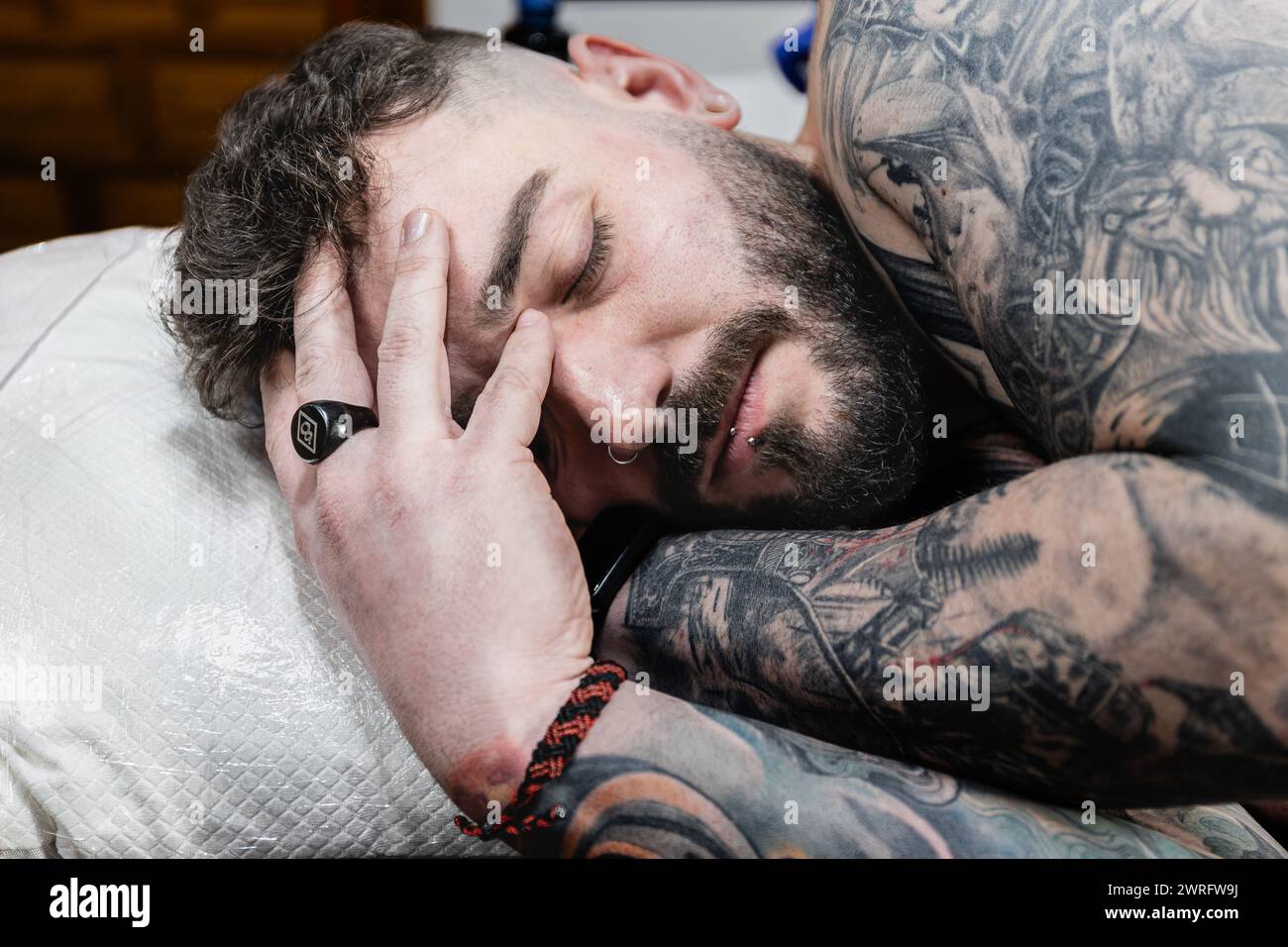 Horizontales Foto ein mit Tattoos bedeckter Mann nimmt sich einen Moment Zeit, um sich auszuruhen. Seine Hand hüllt sanft seinen Kopf und verkörpert die Geduld und Ausdauer, mich zu holen Stockfoto