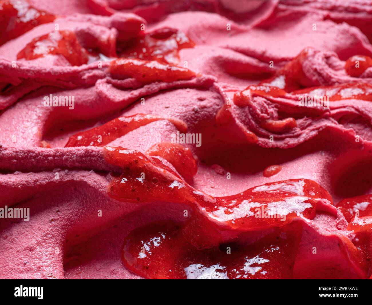 Frozen Strawberry Flavour Gelato - Vollformat Detail. Nahaufnahme einer rosa Oberflächenstruktur von Eiscreme, die mit roten Fruchtstücken bedeckt ist. Stockfoto