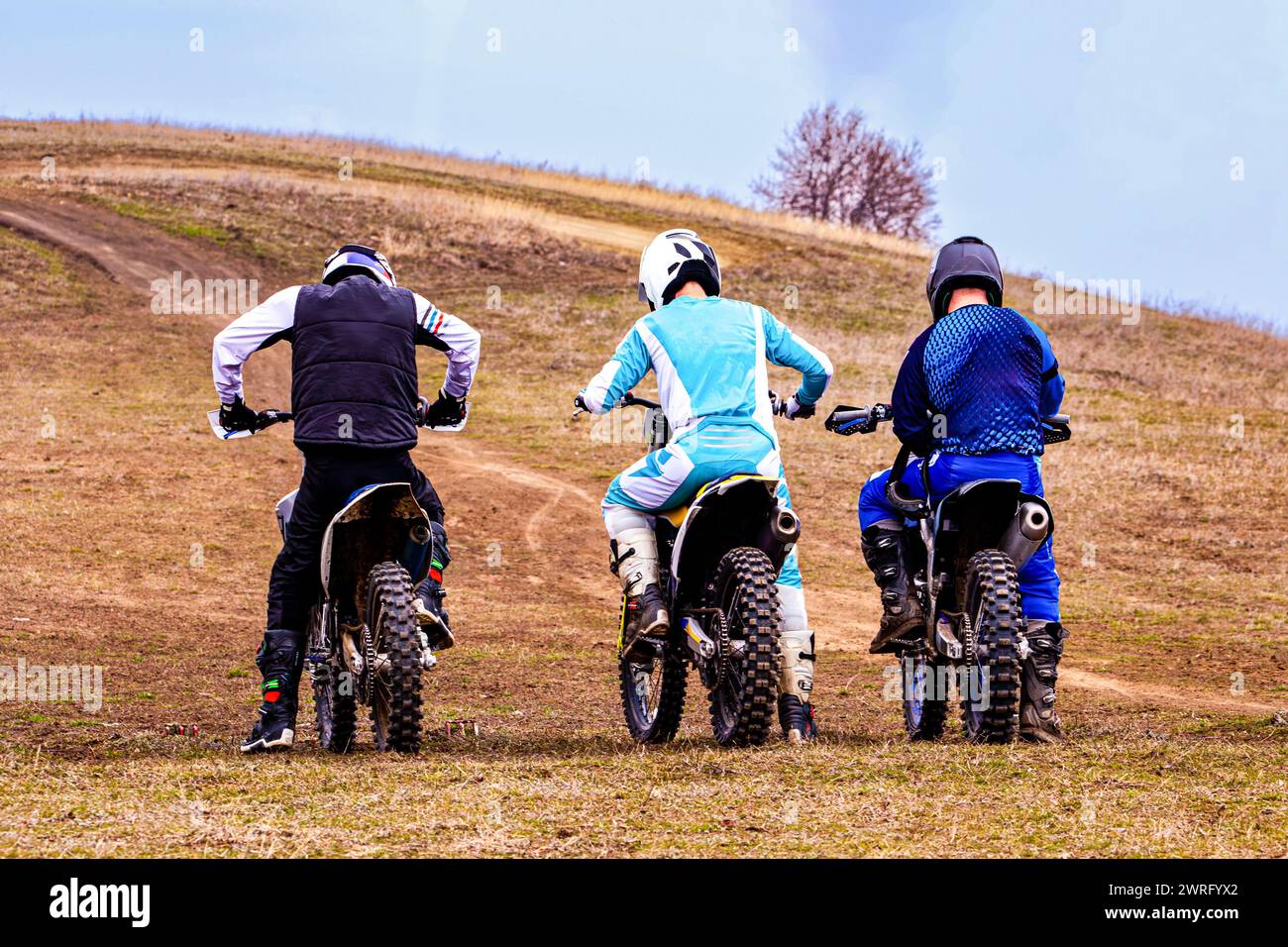 Drei Motorradfahrer fahren mit ihren Fahrrädern auf einer unbefestigten Straße durch ein grasbewachsenes Gelände unter klarem Himmel und tragen Helme aus Sicherheitsgründen Stockfoto