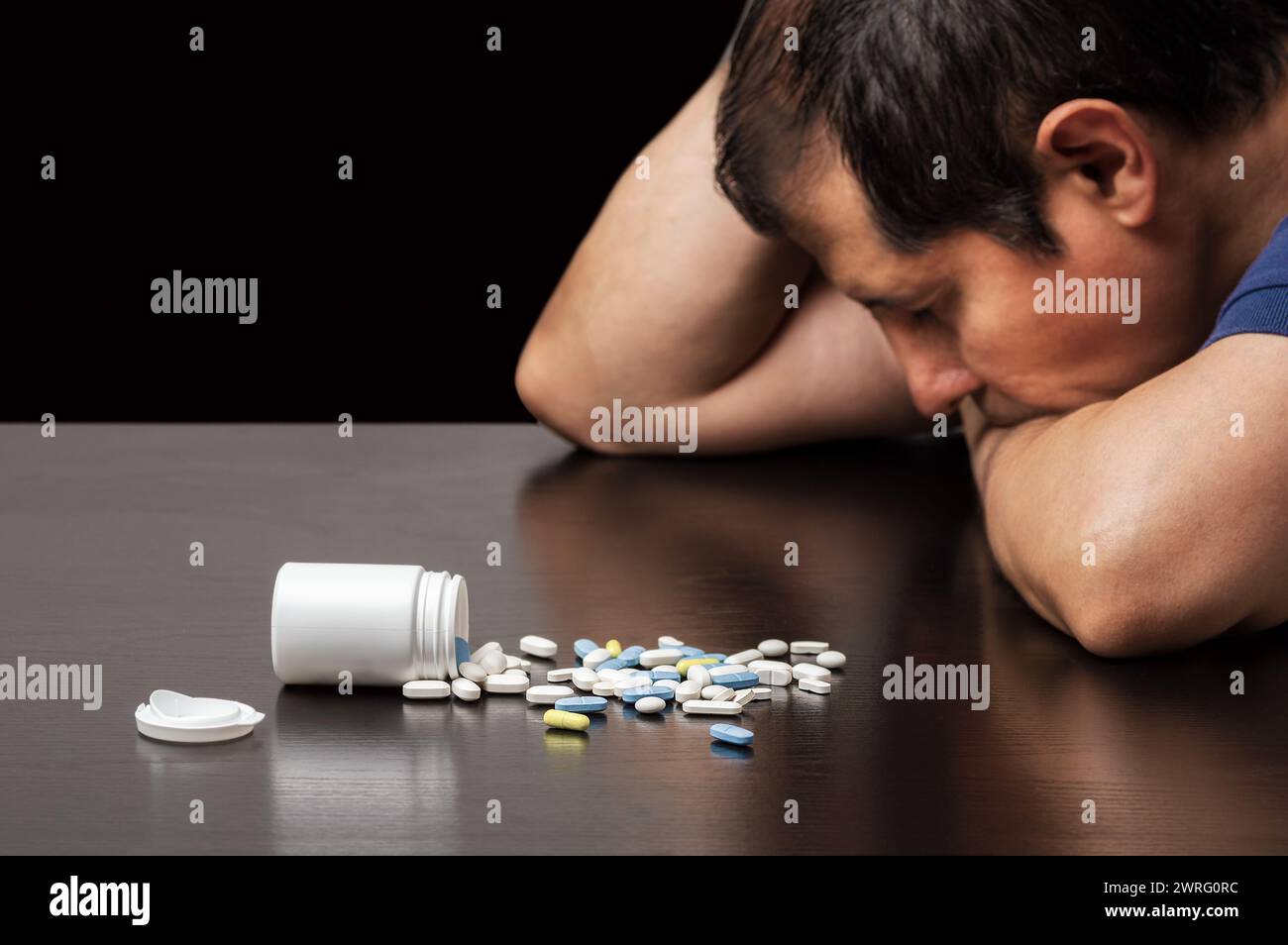 Nahaufnahme eines depressiven Mannes neben vielen Pillen auf einem Tisch auf dunklem Hintergrund Stockfoto