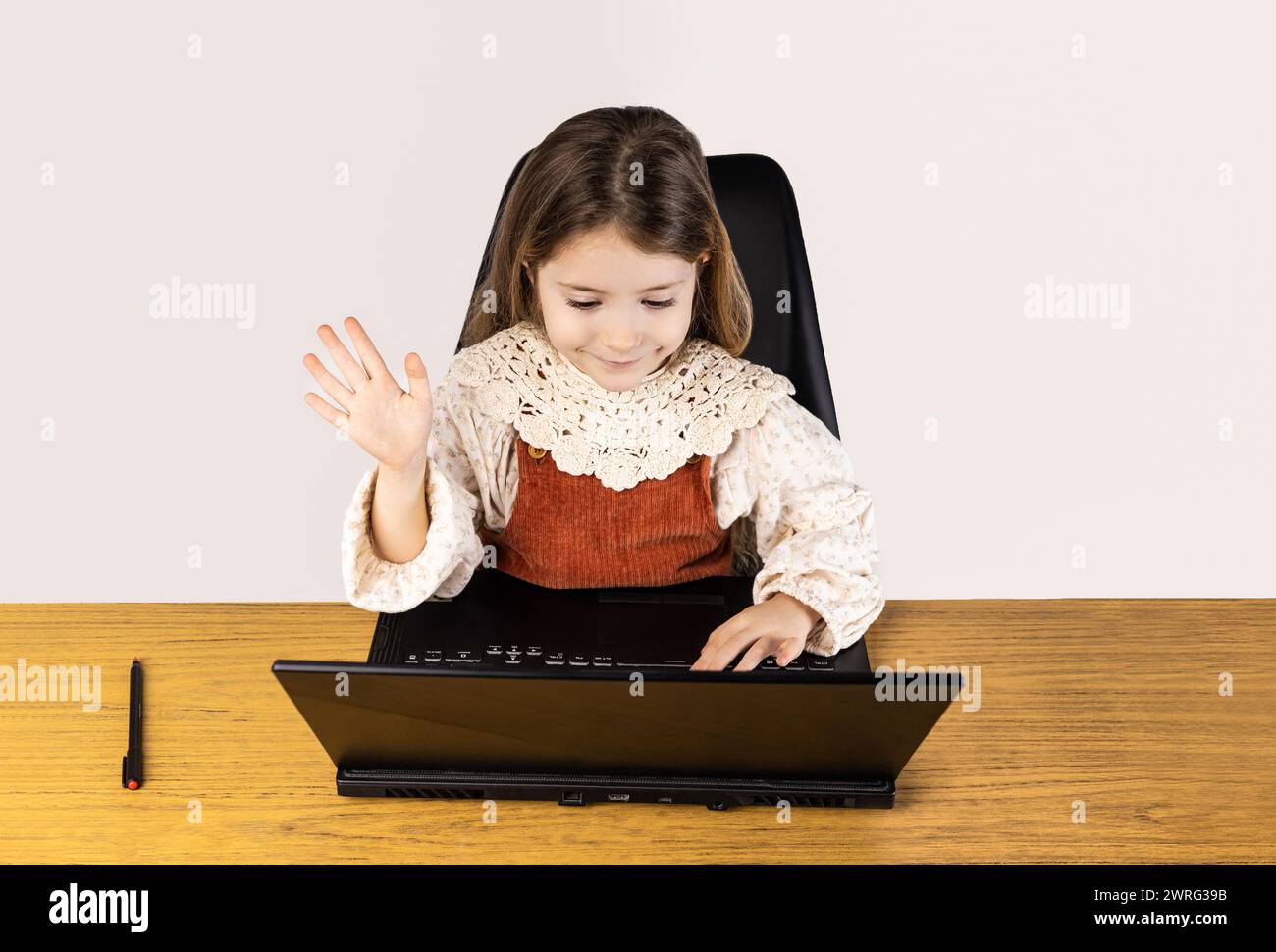 Ein Kleinkind sitzt glücklich auf einem Hartholzboden und benutzt einen Laptop mit einer Hülle. Sie bewegt sich mit Begeisterung auf das Ausgabegerät Stockfoto