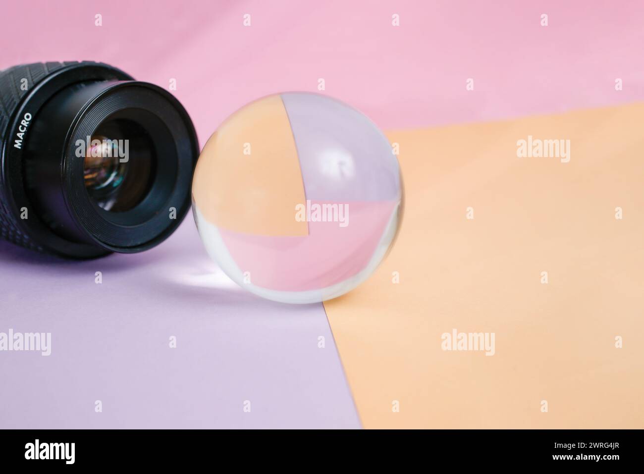 Allgemeines Makroobjektiv-Modell, das durch eine Glaskugel mit Objektiv in beigen und rosa Farben, abstrakter Hintergrund aufnimmt Stockfoto