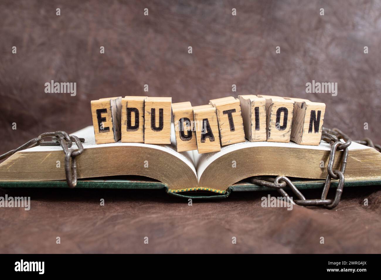 Erziehungswort weiß mit Briefmarken auf Holzblöcken, auf einem geöffneten Buch mit gebrochenen Ketten, das Bildungskonzept repräsentiert Stockfoto