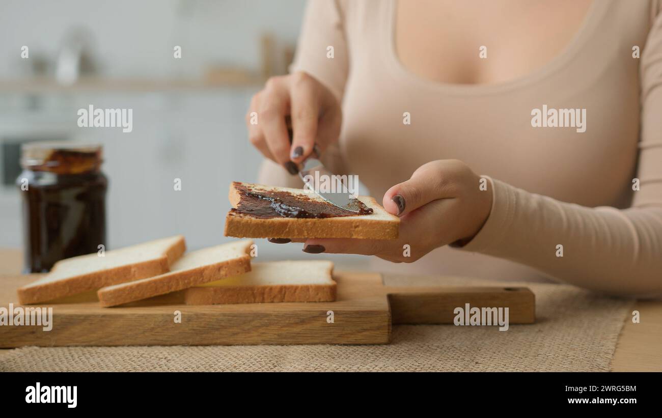 Zugeschnittene Ansicht weibliche Hände verteilen Schokoladenpaste auf Scheiben Toast mit Messer Erdnussbutter auf Brot in Nahaufnahme geben. Unerkennbare Frau in der Küche Stockfoto