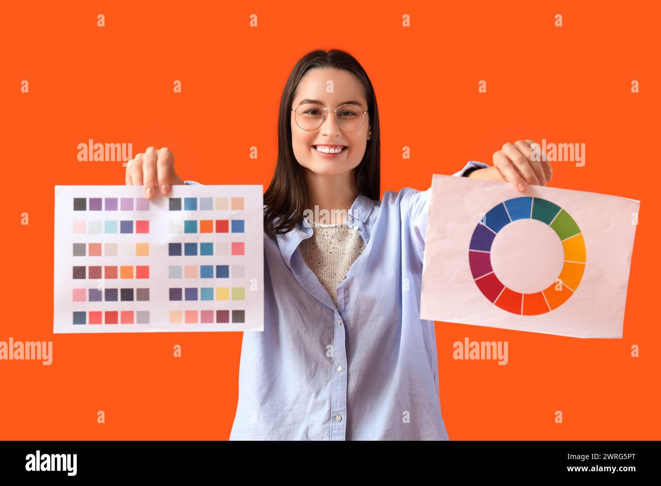 Weibliche Designerin in Brille mit Farbpaletten auf orangem Hintergrund Stockfoto