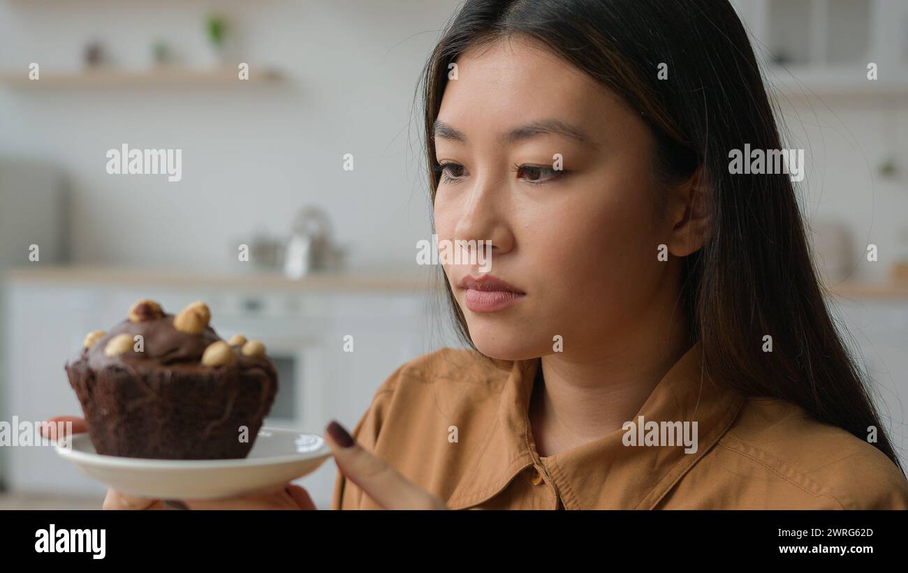 Asiatische koreanische Frau hungriges Mädchen in der Küche halten kalorienreiche Kuchen verweigern Schokolade Dessert zu essen Diät Gewicht verweigern Mehl Gluten süßes Essen nein Stockfoto