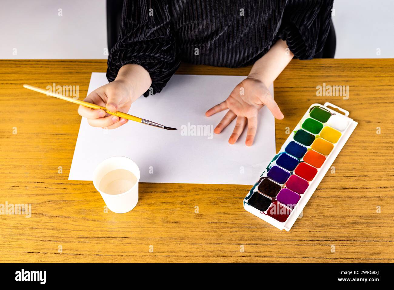 Eine Person hält mit ihrer Hand einen Pinsel, während sie auf ein Blatt Papier malt Stockfoto