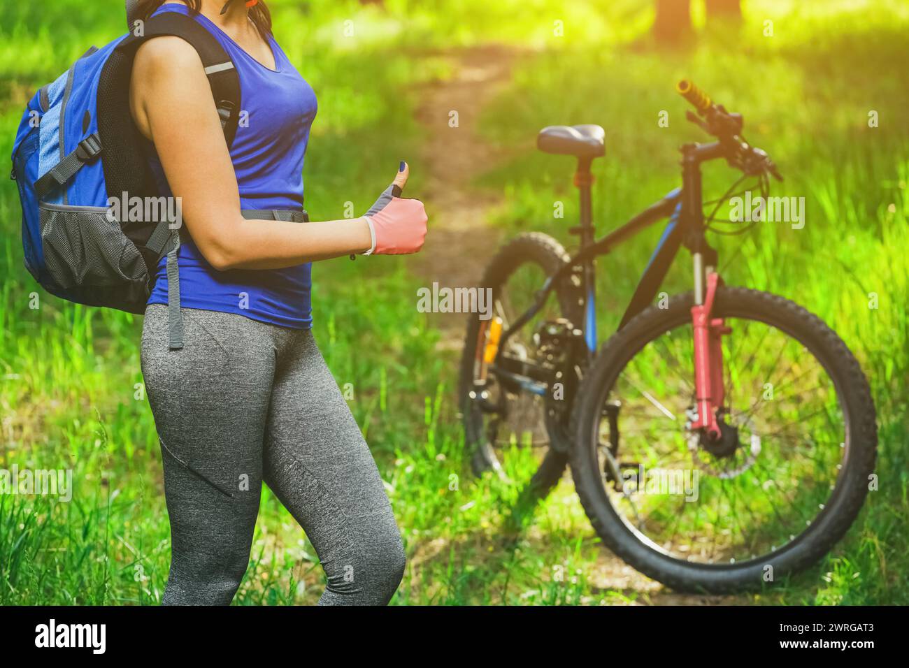 Radfahrerin ist in einem Kiefernwald auf dem Hintergrund Mountainbike und zeigt die Geste eine Klasse. Stockfoto