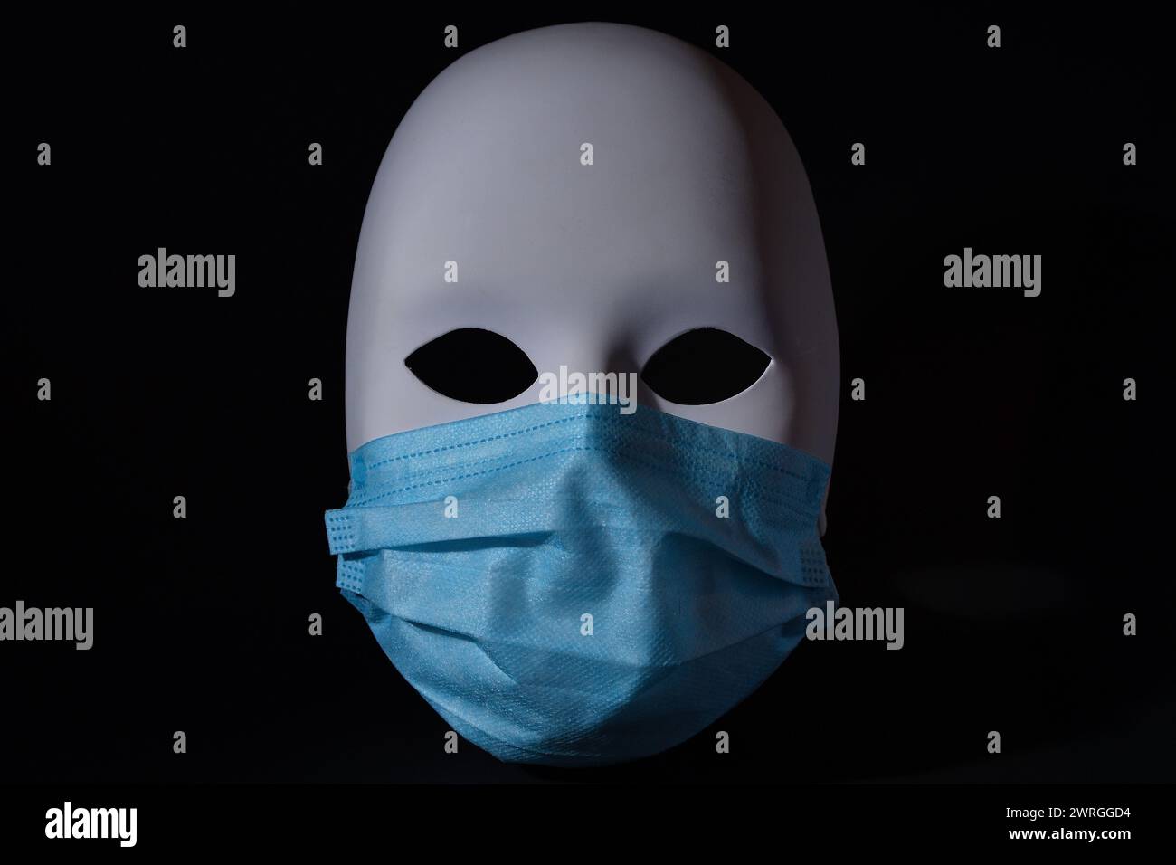 Weiße Theatermaske trägt eine blaue medizinische Schutzmaske, Artiste von Pandemie betroffen, Corona-Virusschutz, die Maske hinter der Maske Stockfoto