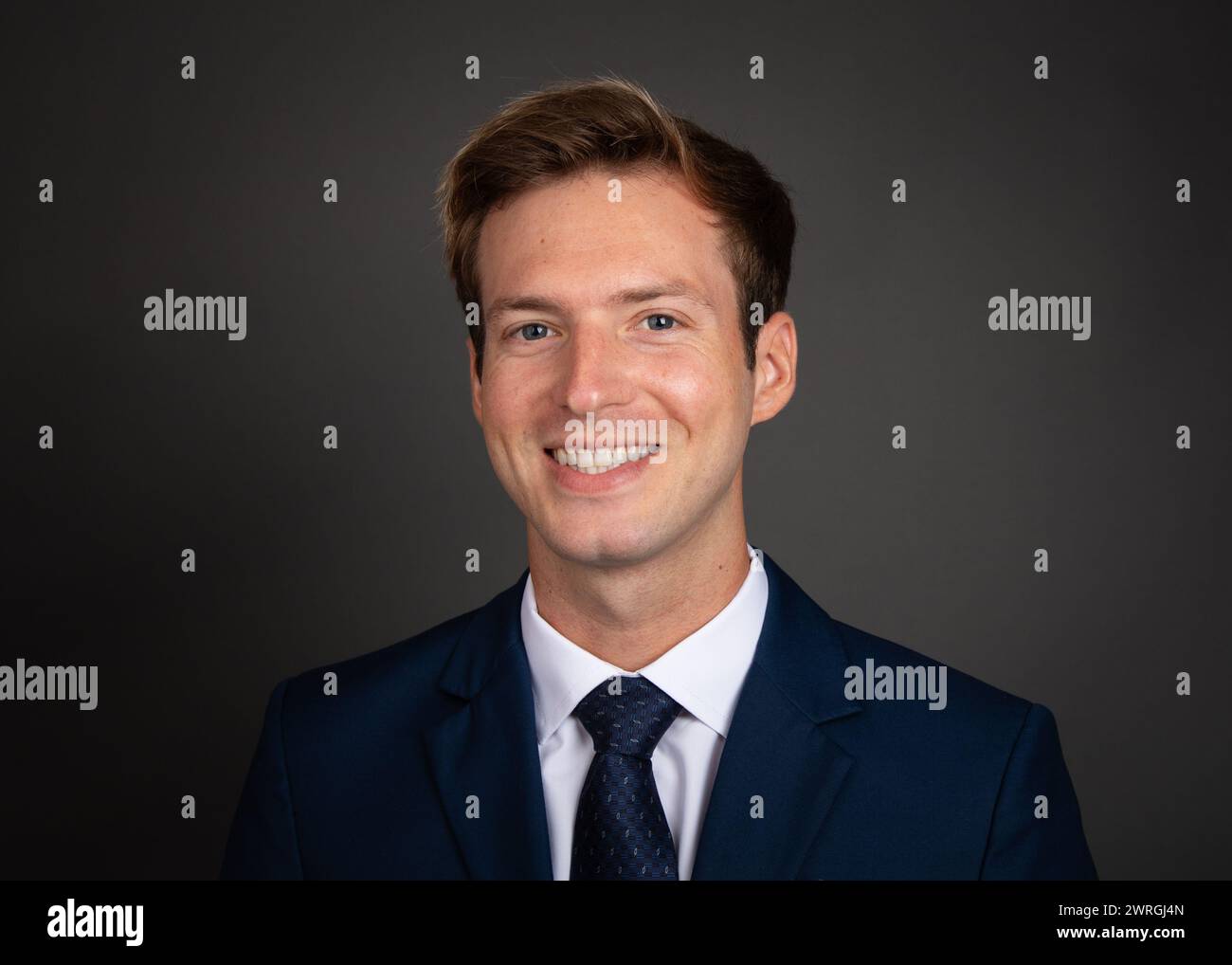 Porträt eines lächelnden Geschäftsmannes in einem Anzug vor grauem Hintergrund Stockfoto