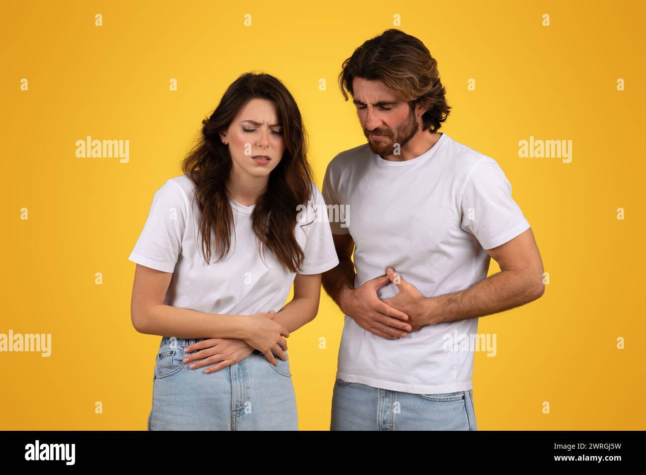 Besorgte Männer und Frauen mit schmerzhaften Ausdrücken, die ihren Magen halten Stockfoto
