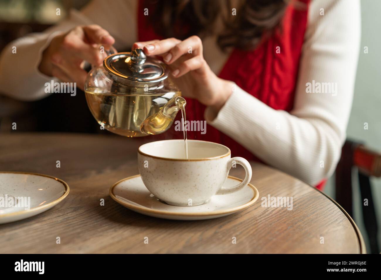 Frau, die an einem Tisch sitzt und Kräutertee in eine Teetasse gießt Stockfoto