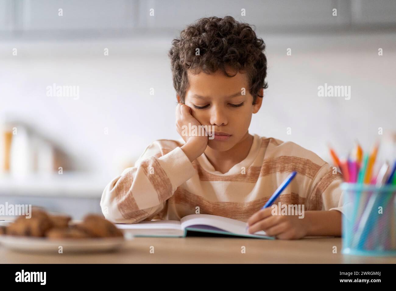 Kleiner schwarzer Junge, der sich müde und schläfrig fühlt, während er seine Hausaufgaben macht Stockfoto