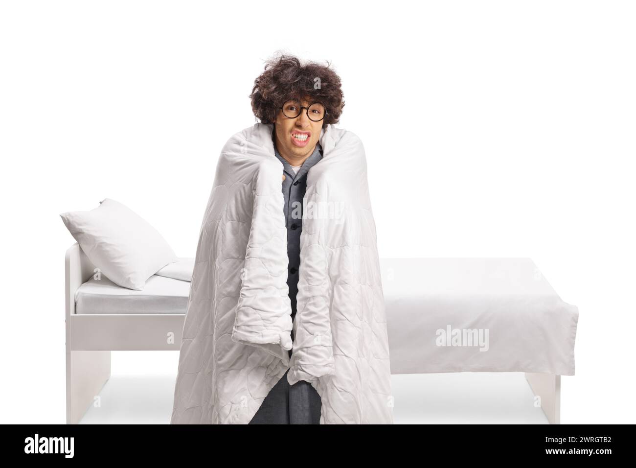 Junger Mann in eine Decke gewickelt, der vor einem Bett auf weißem Hintergrund steht Stockfoto
