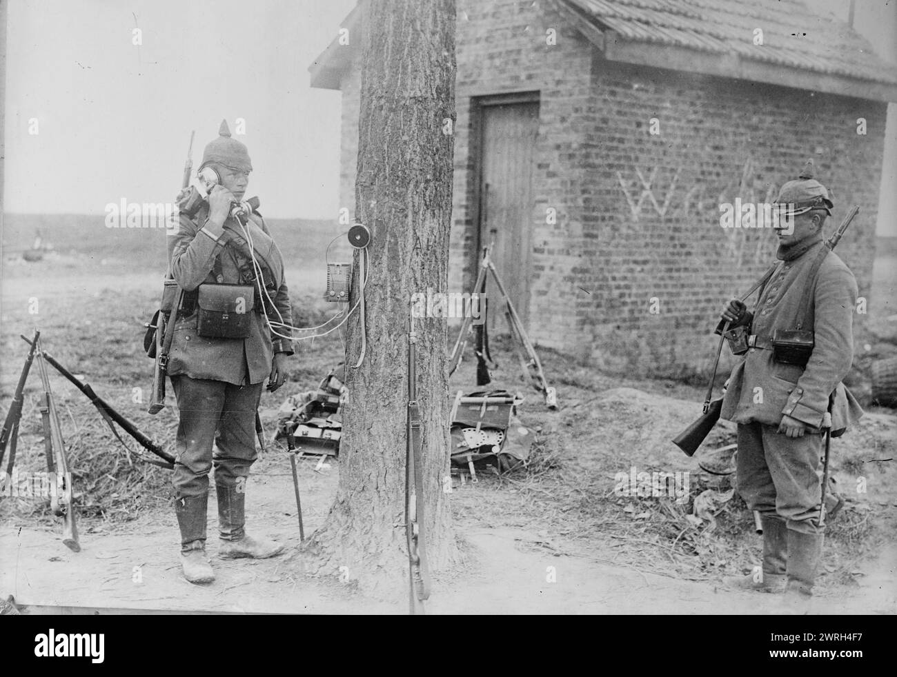 Deutsches Feldtelefon, 1914. Deutscher Soldat telefoniert am Telefon, der an einem Baum neben einem Backsteingebäude befestigt ist, während des Ersten Weltkriegs Stockfoto