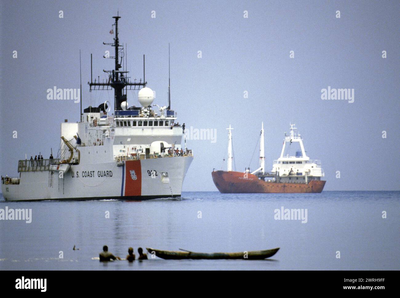 18. Mai 1994;Port-au-Prince, Haiti-Ein Schiff der US-Küstenwache patrouilliert im Hafen von Port-au-Prince, Haiti, während ein örtlicher Fischer seinen Fang bearbeitet. Stockfoto