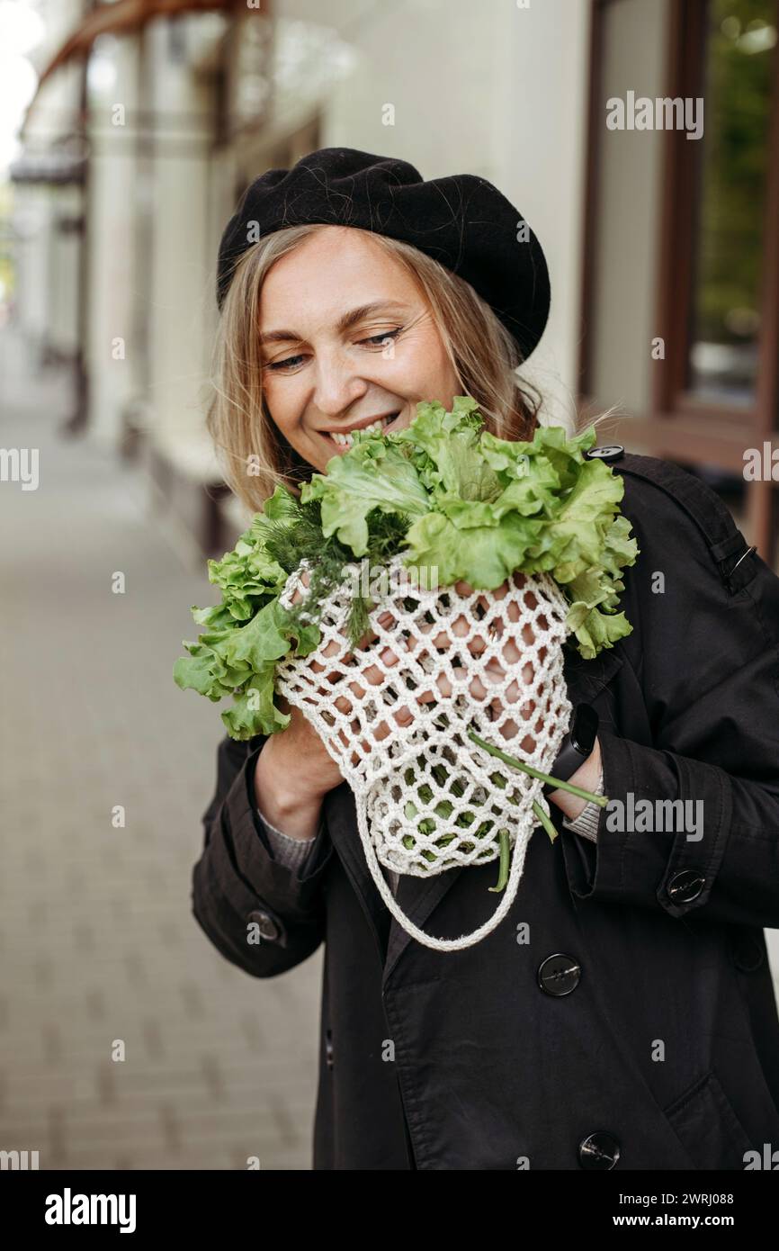 Eine Frau, die steht und einen Haufen Salat vor ihrem Gesicht hält. Vertikales Bild. Stockfoto