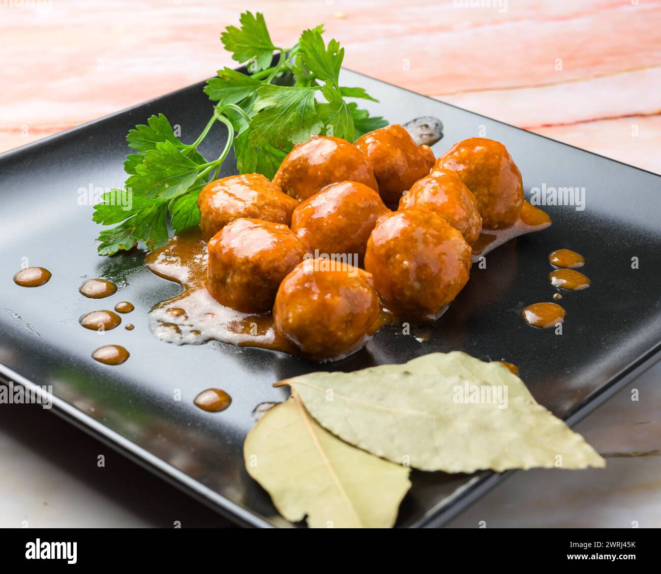 Glasierte Fleischbällchen garniert mit Petersilie und Lorbeerblatt auf einem schwarzen Teller, typisches Essen, typisch mediterrane mallorquinische Küche typisch von balearen Stockfoto