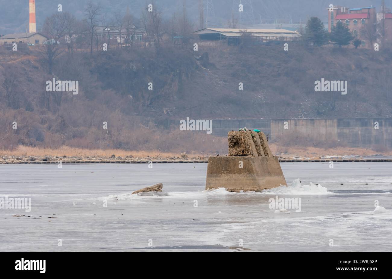 Betonsäulensockel einer unfertigen Brücke, die am grauen Wintermorgen in der Provinz Gyeonggi in Südkorea durch die Oberfläche des gefrorenen Flusses ragt Stockfoto