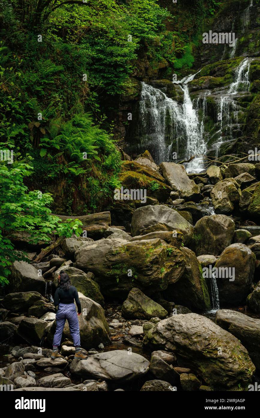 Junge Wanderer auf Felsbrocken am Torc Waterfall im Killarney National Park, County Kerry, Irland Stockfoto