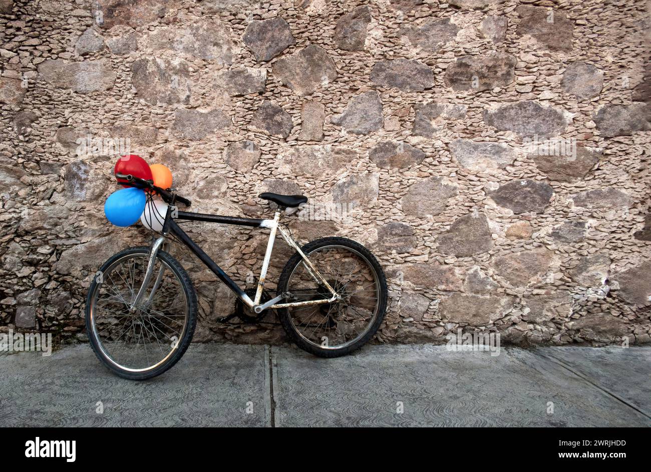 Ein altes Fahrrad mit bunten Ballons auf einer alten Felsmauer in Mexiko, mit Platz für Text Stockfoto