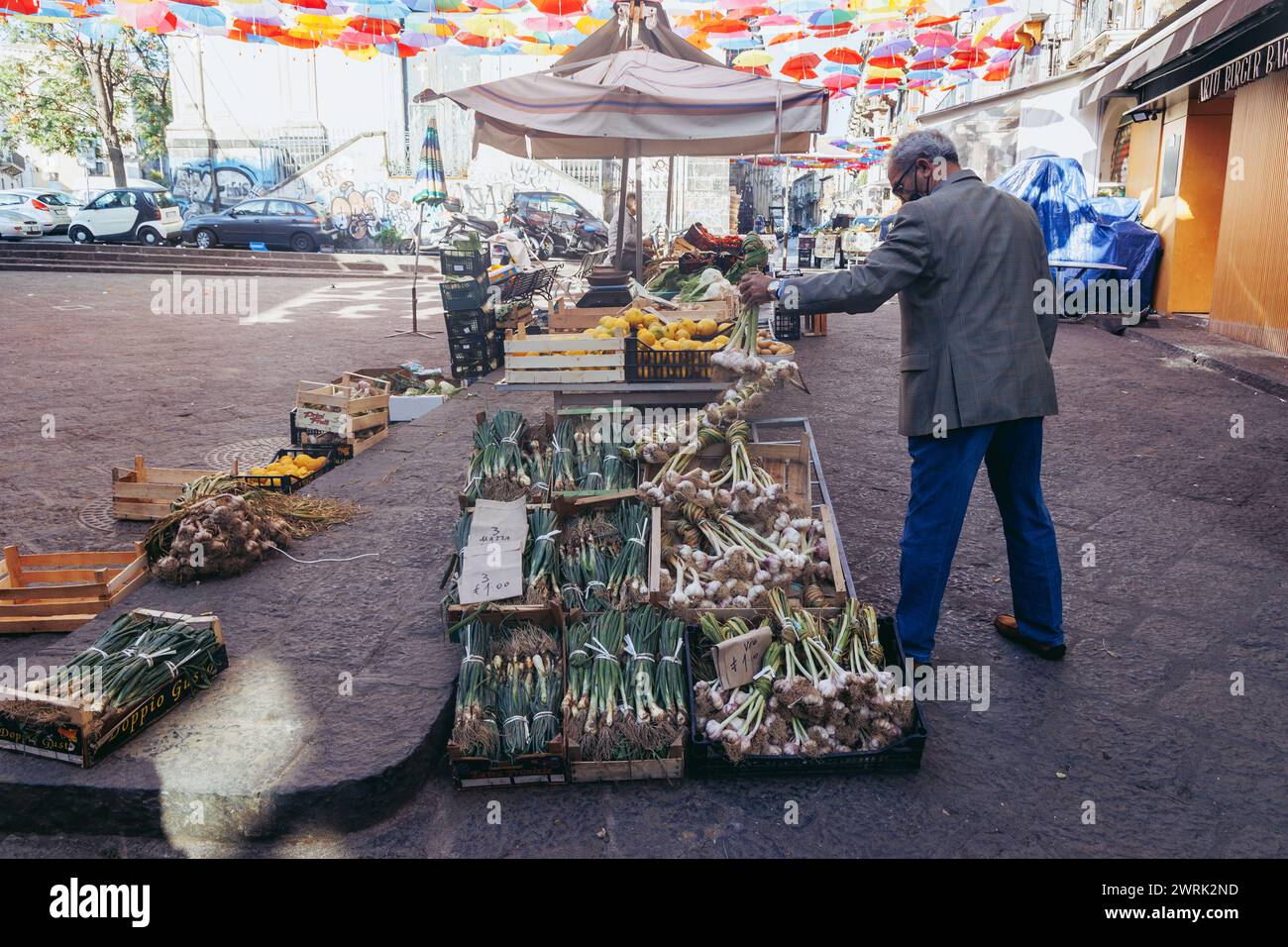 Mann, der Knoblauch und Schnittlauch auf dem Markt in der Altstadt in Catania auf der Insel Sizilien verkauft Stockfoto