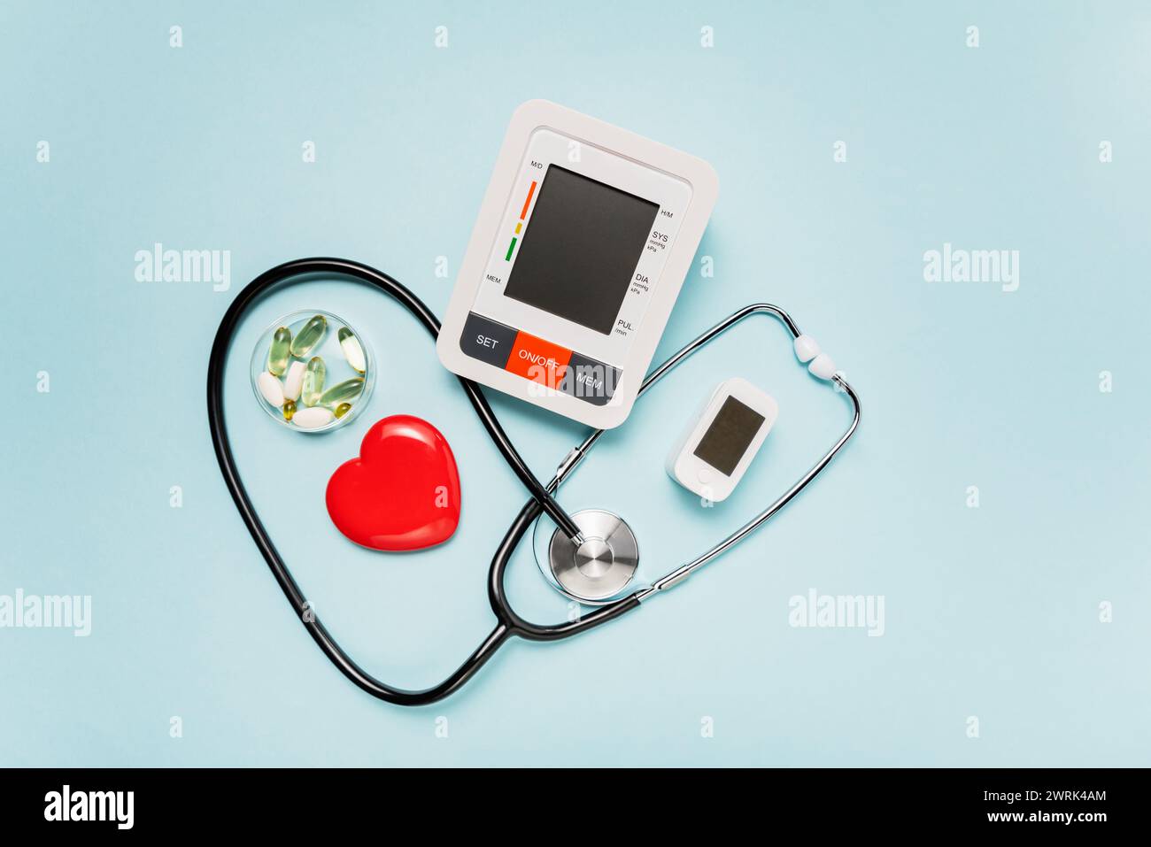 Stethoskop, Herzmodell, Pillen und digitale Geräte auf blassblauem Hintergrund symbolisieren Liebe und Pflege im medizinischen Bereich. Stockfoto