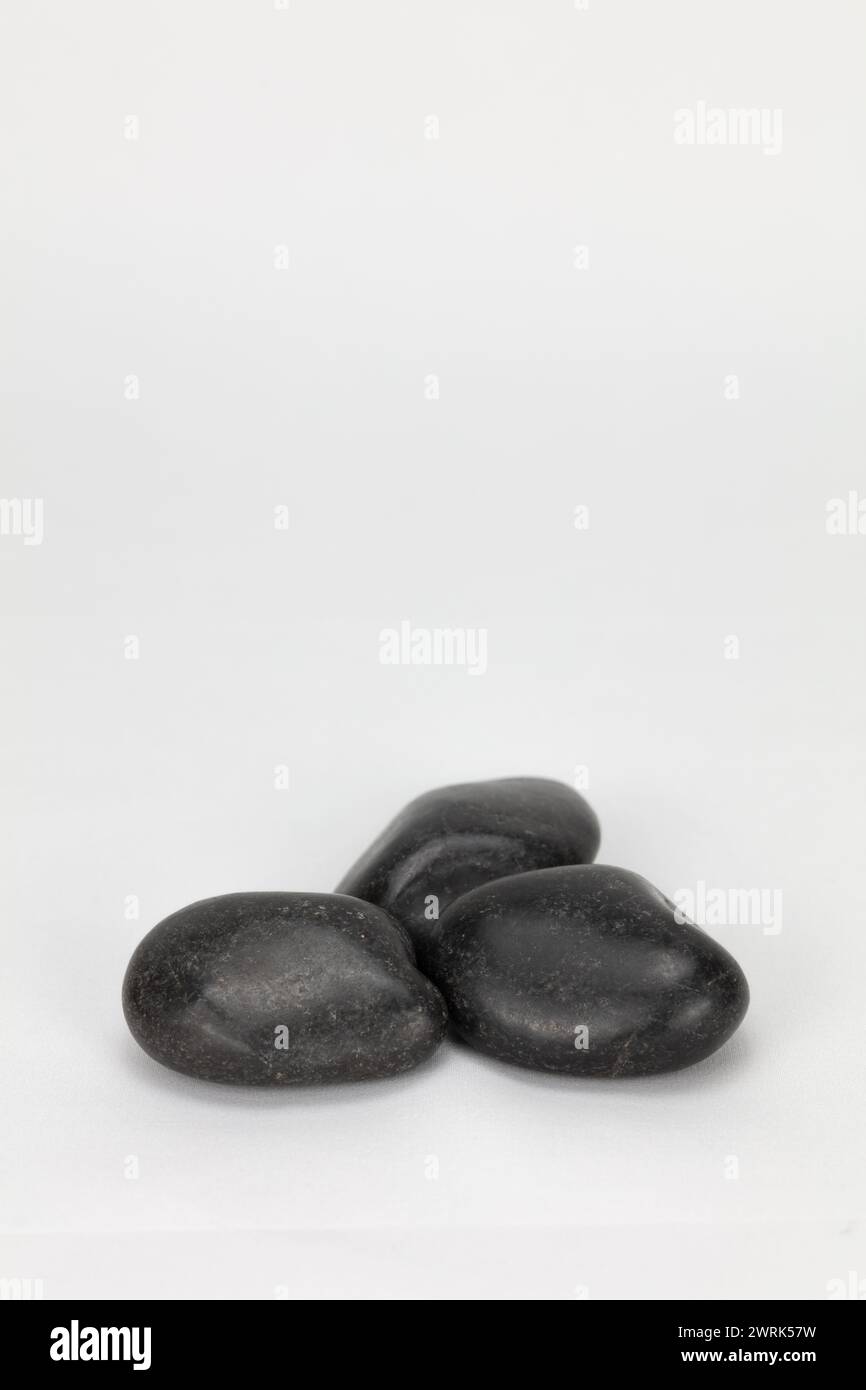 Drei schwarze Kieselsteine vor einem blass bearbeitbaren Hintergrund, die in hochauflösender und bearbeitbarer Porträtgröße aufgenommen werden können, können im Composite mit Kopierraum verwendet werden Stockfoto