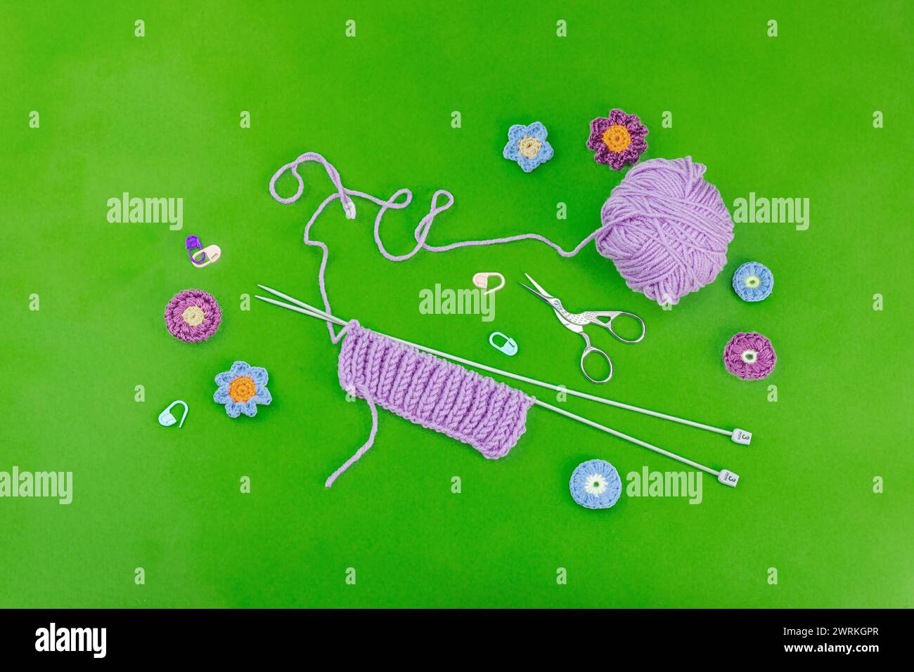 Frühjahrstrickkonzept. Musterbeispiel, traditionelle Werkzeuge, Garnknäuel, Häkelblumen. Kreative handgemachte flache Lay, hellgrüner Hintergrund, Oberseite Stockfoto