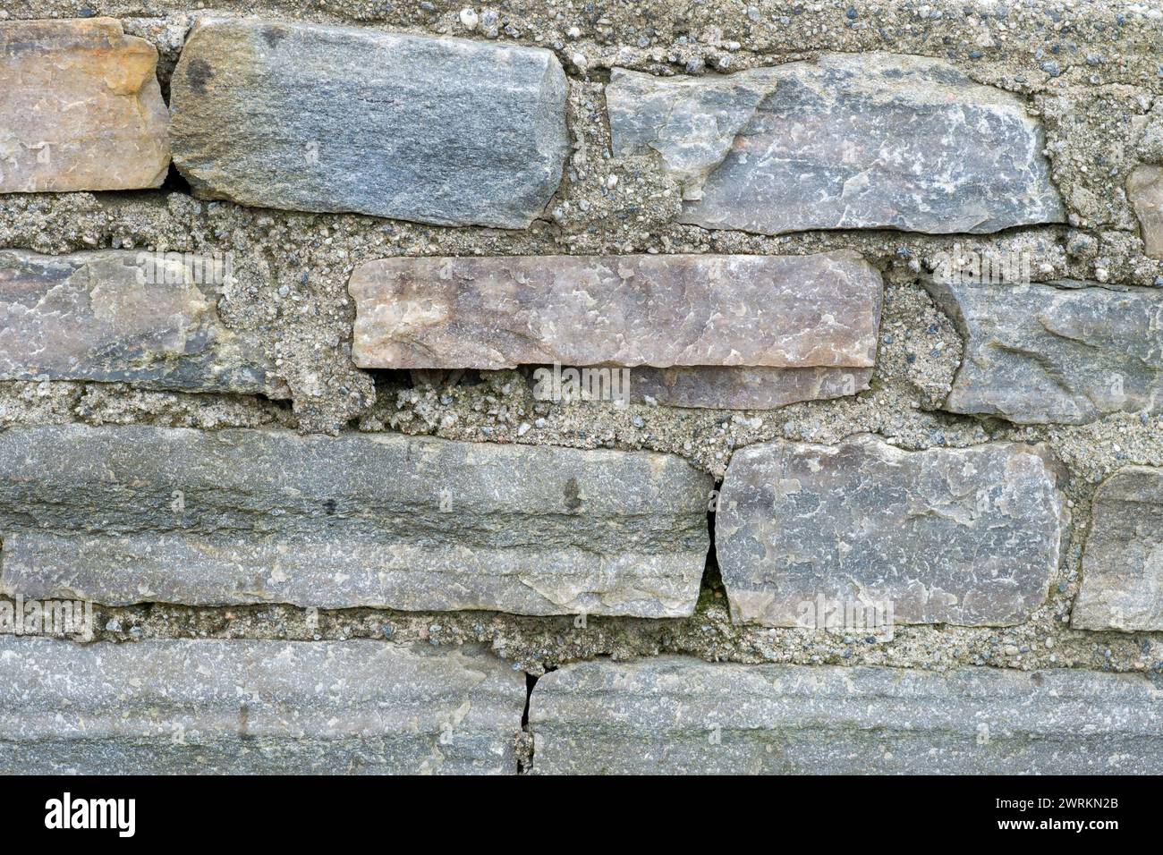 Ein detaillierter Blick auf die vielfältigen Texturen und Farben von alten Steinen in einer Wand, die bei Tageslicht erfasst werden. Stockfoto