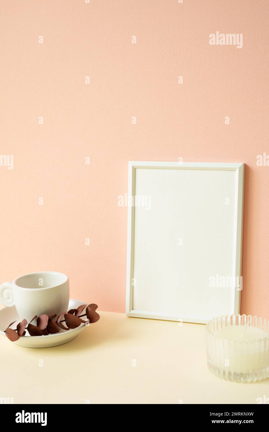 Weißer leerer Bilderrahmen mit Kaffeetasse, Kerze auf elfenbeinfarbenem Tisch. Pinkfarbener Wandhintergrund Stockfoto