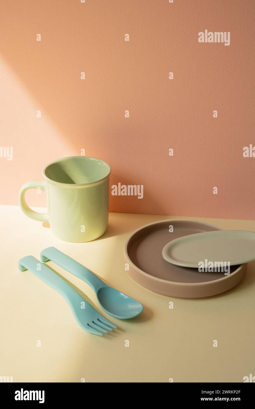 Küchenbesteck Gabel und Löffel, Becher, Geschirrteller auf elfenbeinfarbenem Regal. Pinkfarbener Wandhintergrund Stockfoto