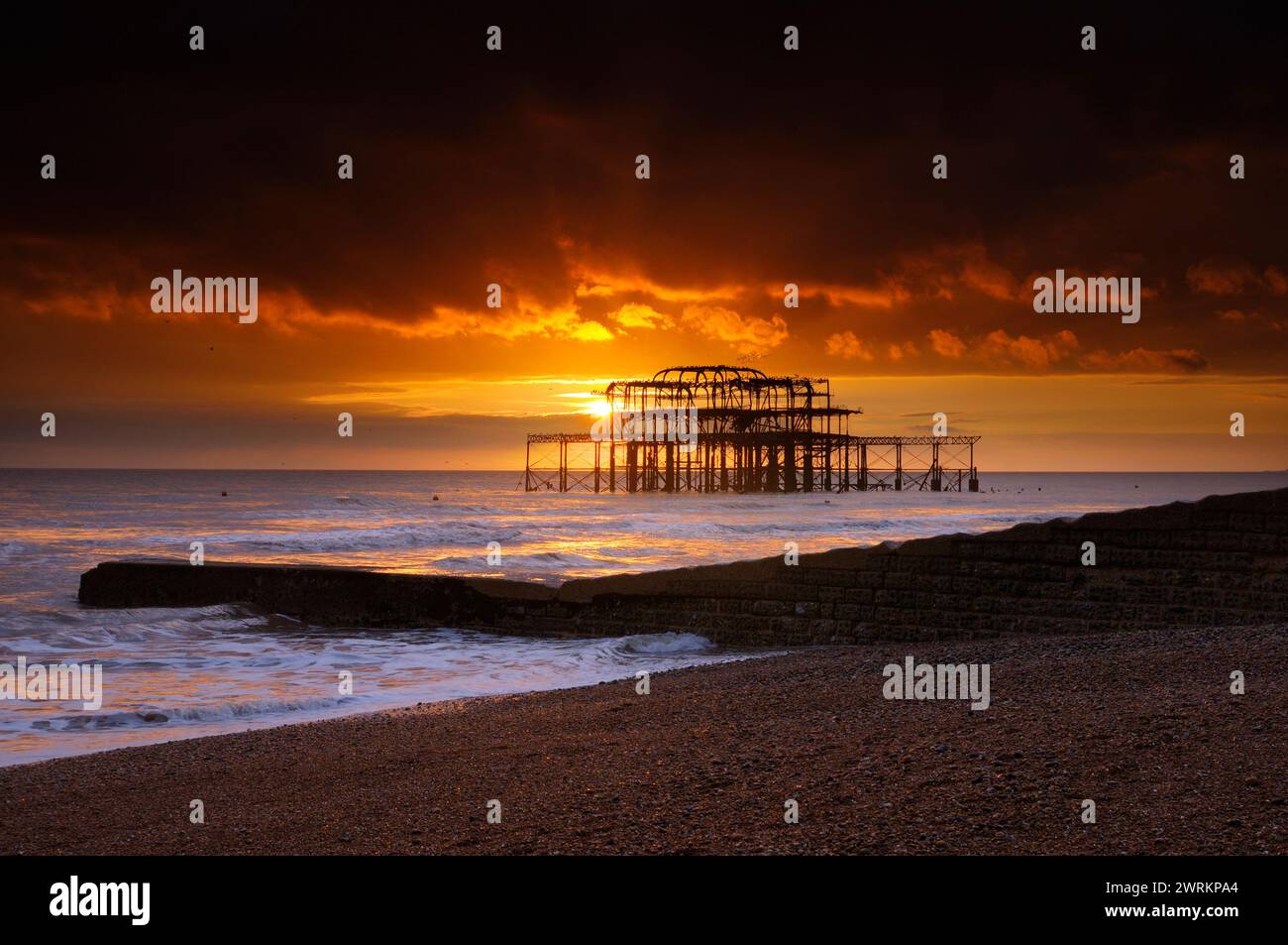 Ein wunderschöner orangener Sonnenuntergang hinter den Ruinen des Brighton West Pier im Meer von der Schindelküste von Brighton Beach, Brighton and Hove, East Sussex, UK 2024 Stockfoto