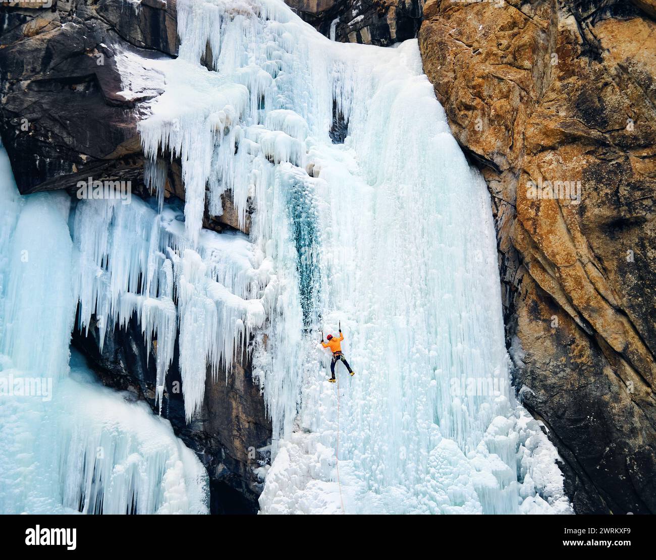 Luftaufnahme eines Athleten in orangefarbener Jacke Eisklettern am großen gefrorenen Wasserfall in der Barskoon-Schlucht im Bergtal in Kirgisistan Stockfoto