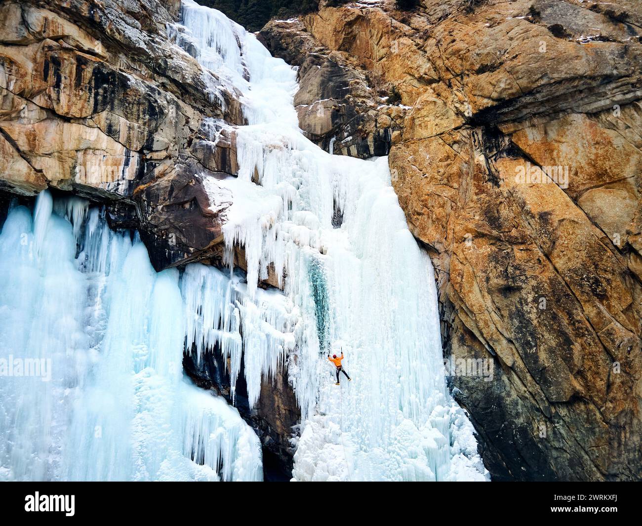 Luftaufnahme eines Athleten in orangefarbener Jacke Eisklettern am großen gefrorenen Wasserfall in der Barskoon-Schlucht im Bergtal in Kirgisistan Stockfoto