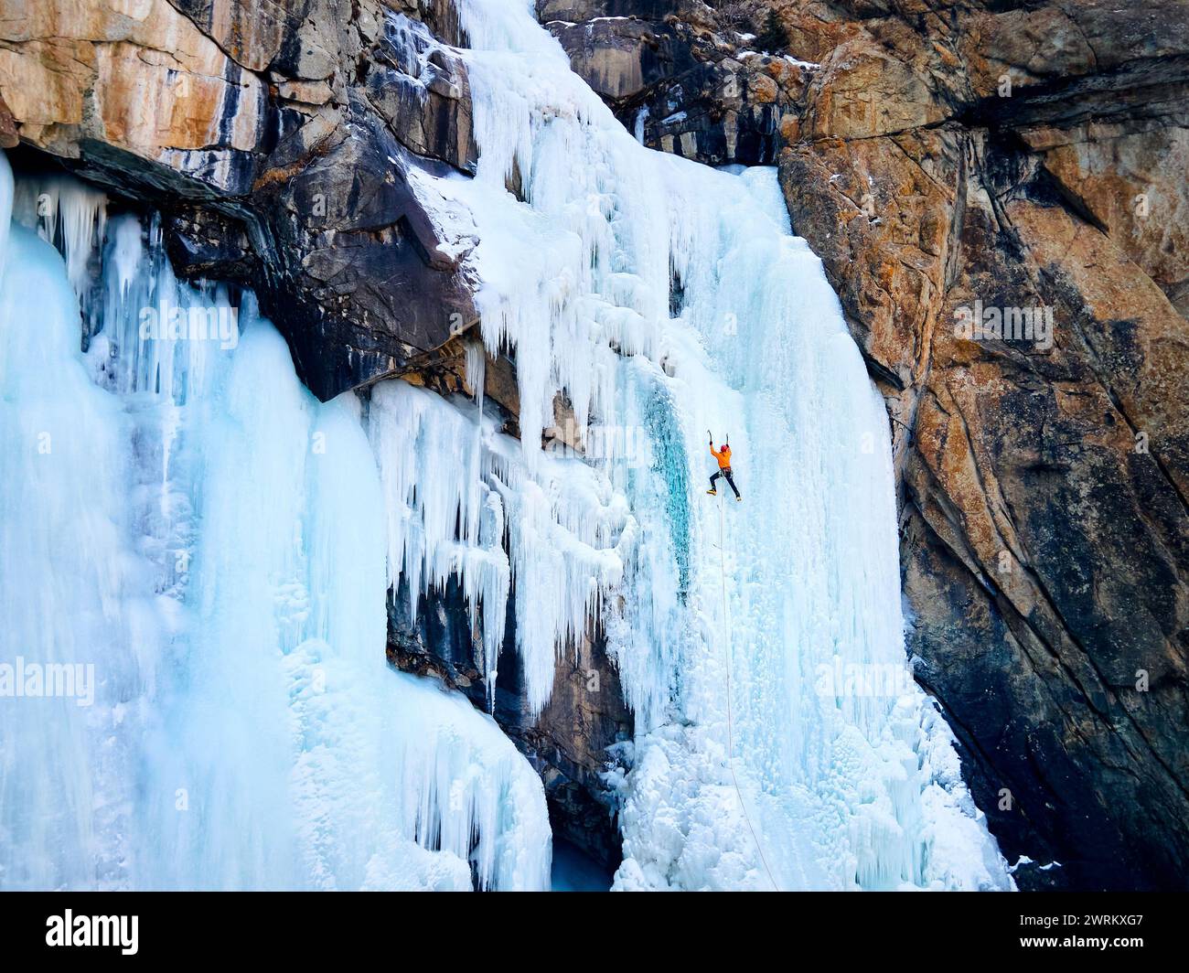 Luftaufnahme eines Athleten in orangefarbener Jacke Eisklettern am großen gefrorenen Wasserfall in der Barskoon-Schlucht im Bergtal in Kirgisistan Stockfoto