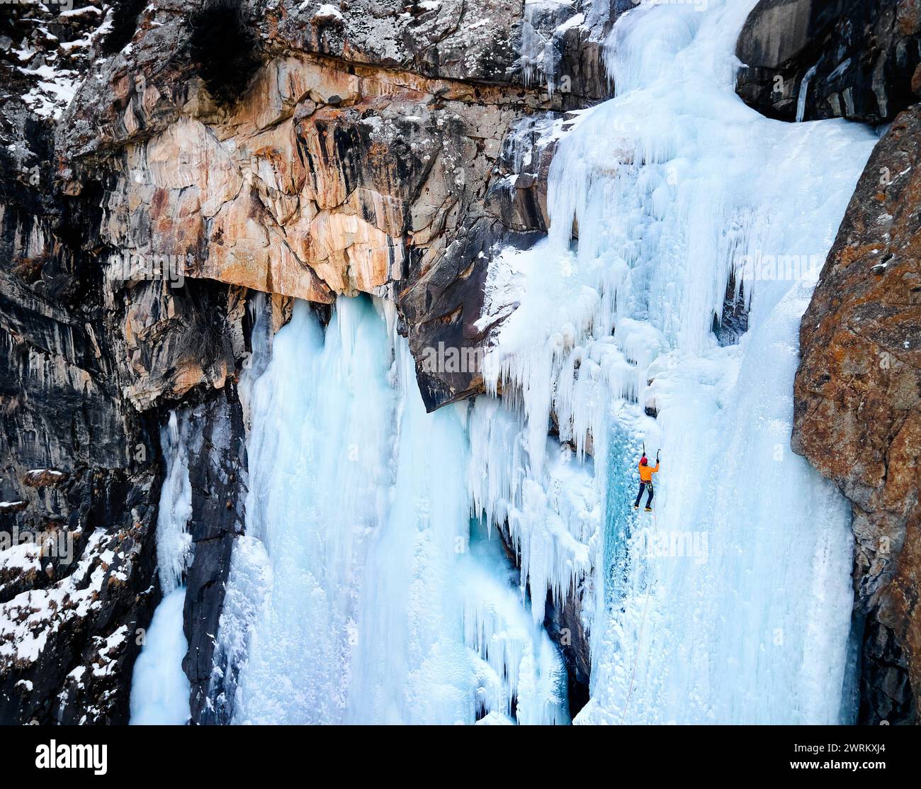 Luftaufnahme eines Athleten in orangefarbener Jacke Eisklettern am großen gefrorenen Wasserfall in der Barskoon-Schlucht im Bergtal in Kirgisistan Stockfoto