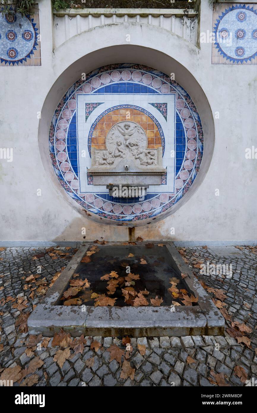 Fonte dos Pisões Brunnen mit Trinkwasser in Sintra, Portugal. Springbrunnen aus dem Jahr 1931 mit Fliesenplatte und Steinrelief von Kindern mit Tassen und p Stockfoto