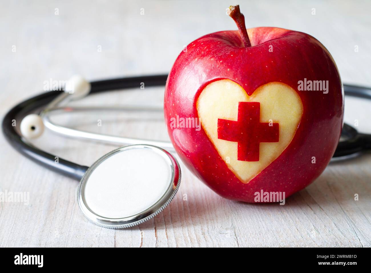 Apfel mit geschnitztem medizinischem Kreuz im Herzen mit Stethoskop, kreativem Gesundheits- und Pflegekonzept Stockfoto