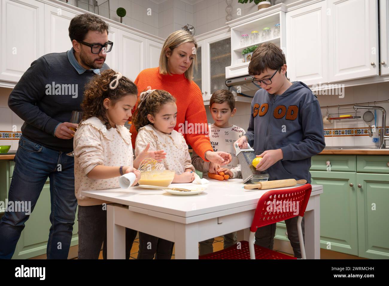 In der Küche versammelt sich eine generationenübergreifende Familie, die gemeinsam eine Mahlzeit zubereitet, wobei Kinder und Erwachsene aktiv beteiligt sind. Stockfoto