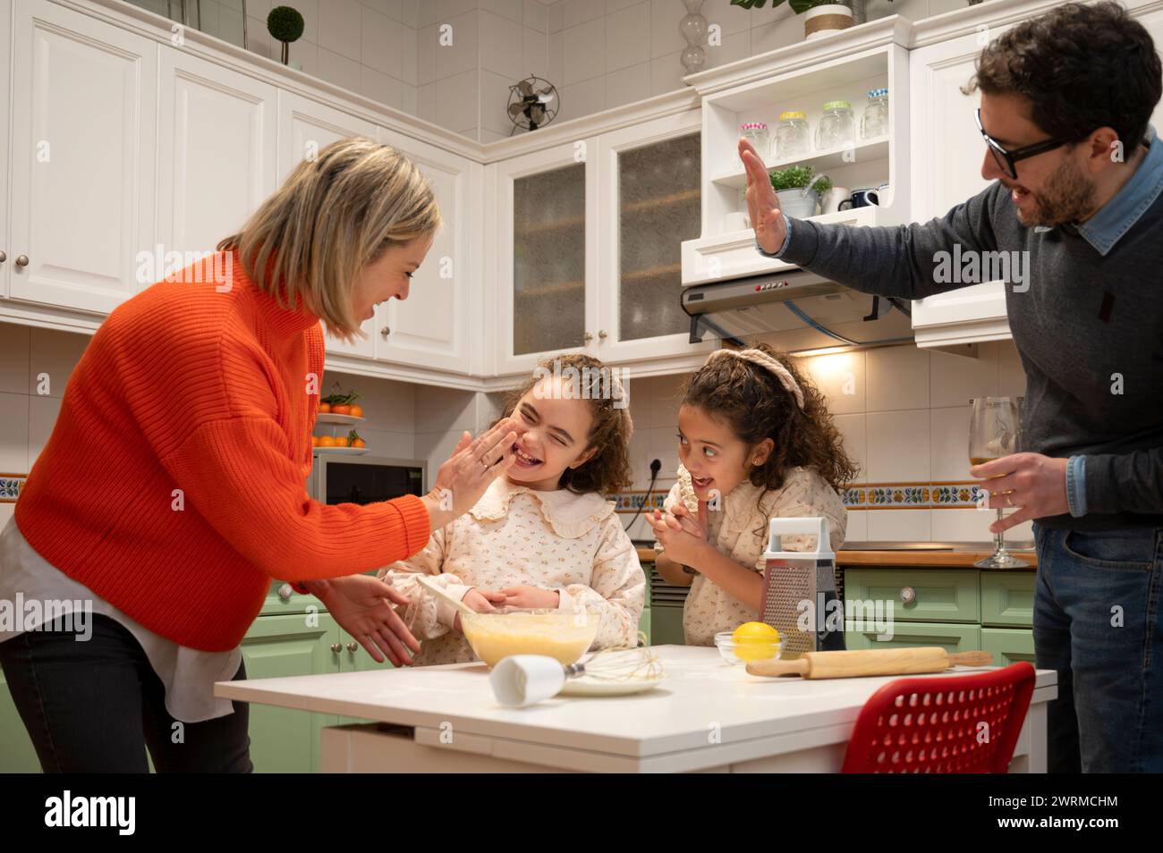 Die Familie versammelt sich in einer Küche, lacht und bereitet gemeinsam Essen zu, was eine heimelige Atmosphäre und familiäre Bindung zum Ausdruck bringt. Stockfoto