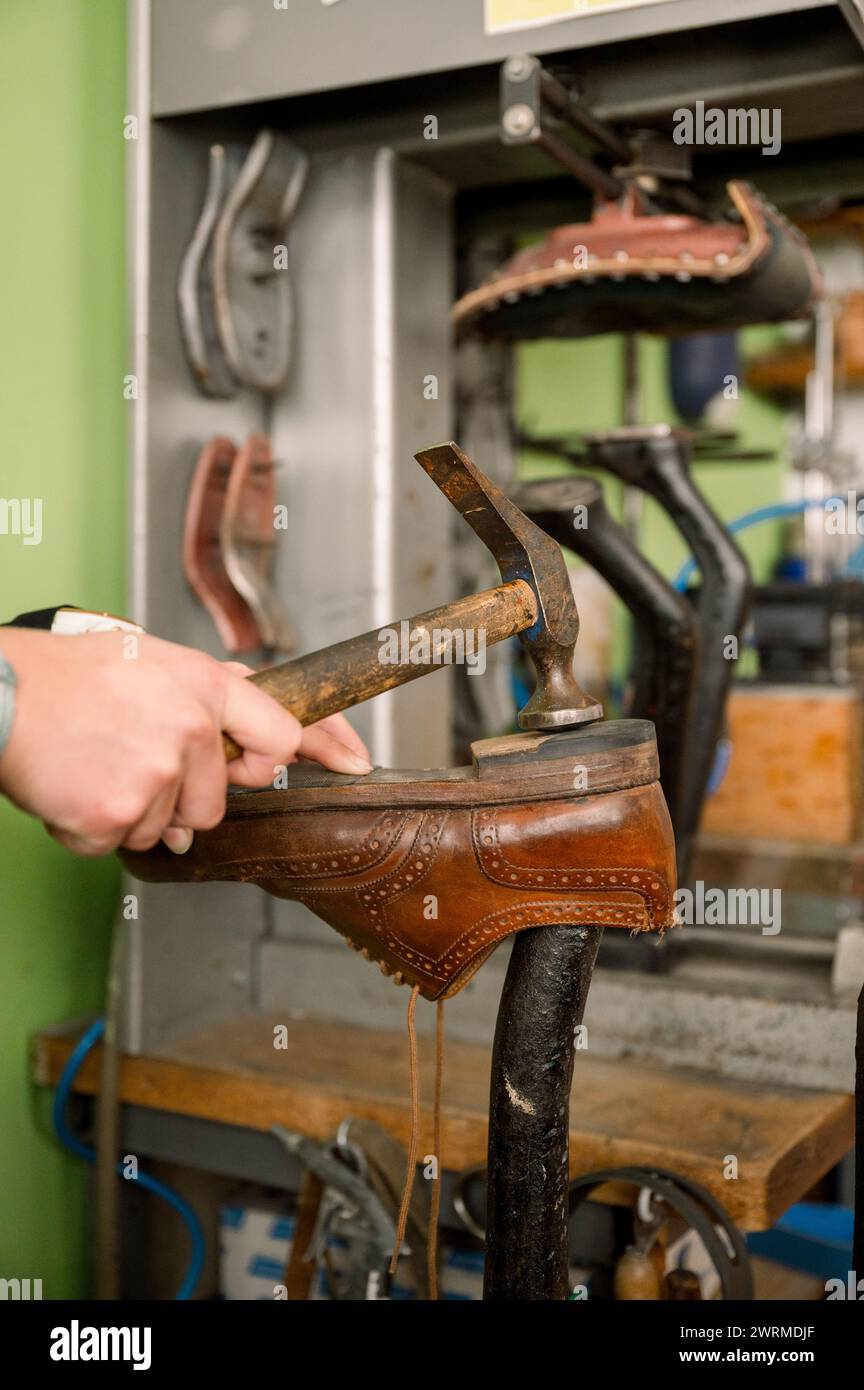 Eine abgeschnittene, nicht erkennbare Handwerkerhand, die in einer Schuhmacherwerkstatt in Österreich auf eine Schuhsohle hämmert, zeigt die Kunst der traditionellen Schuhherstellung. Stockfoto