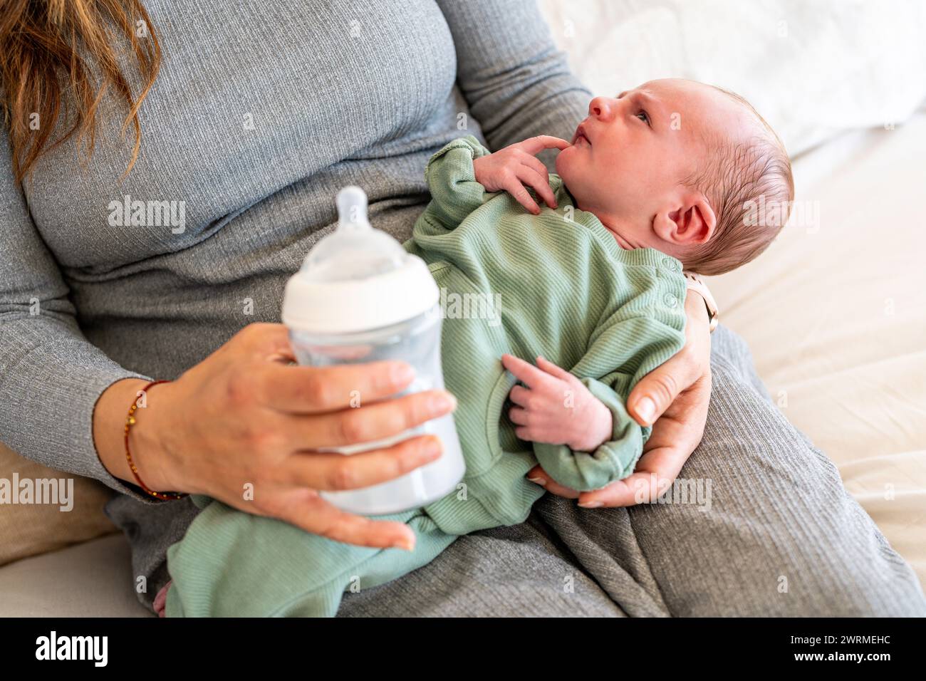 Ein neugeborenes Baby schaut auf, während es mit einer Flasche gefüttert wird, in den Armen der anonymen Mutter, eine Szene der frühen Lebensernährung und mütterlichen Bindung Stockfoto