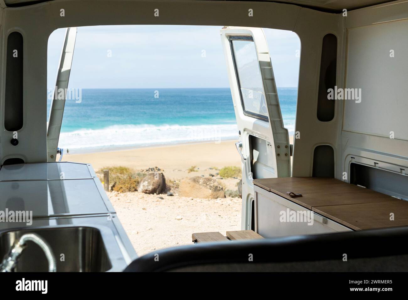 Erleben Sie Ruhe durch die offene Rückseite eines Vintage-Minibusses mit Blick auf eine ruhige Strandszene. Stockfoto