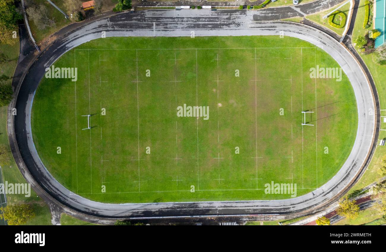 Aus der Vogelperspektive eines grünen Rugbyfeldes mit weißen Markierungen, umgeben von einer Rennstrecke. Stockfoto