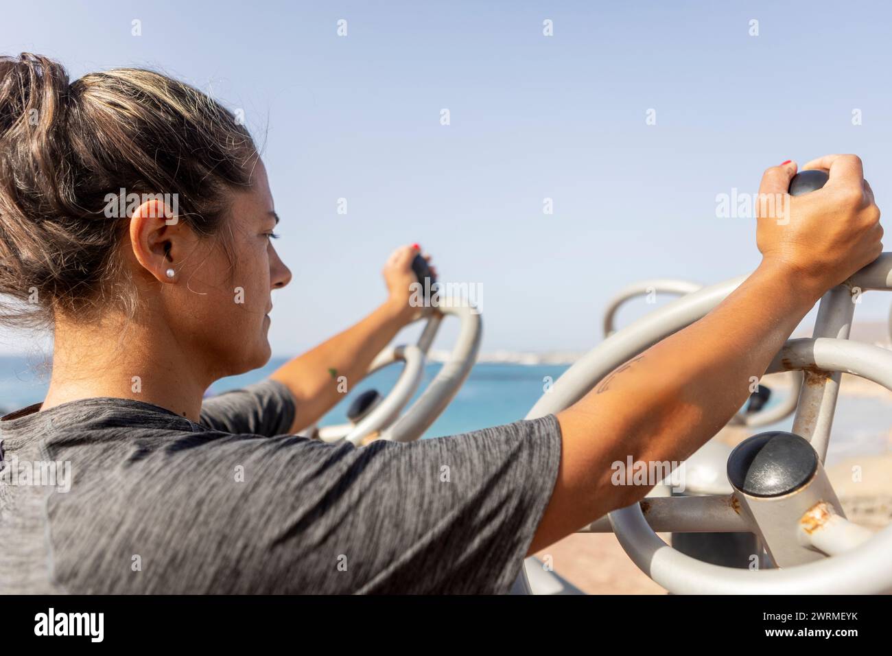 Frau mit seitlicher Ansicht übt an Fitnessgeräten in einem Outdoor-Fitnessstudio am Strand aus. Stockfoto