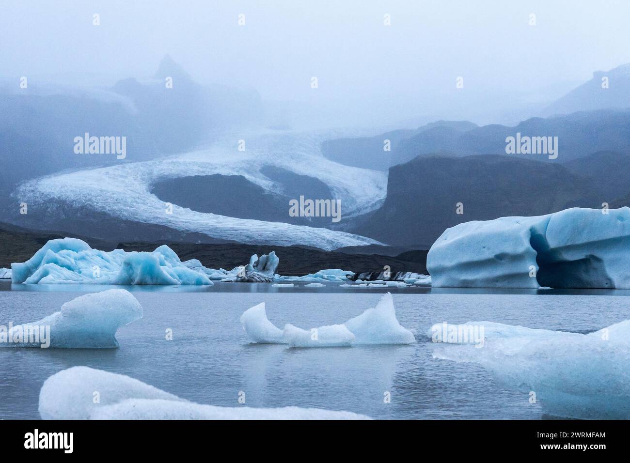Eisberge treiben in den stillen Gewässern einer Gletscherlagune mit Vatnajokulls in Nebel gehülltem Eisschild und fangen Islands ätherische Schönheit ein Stockfoto