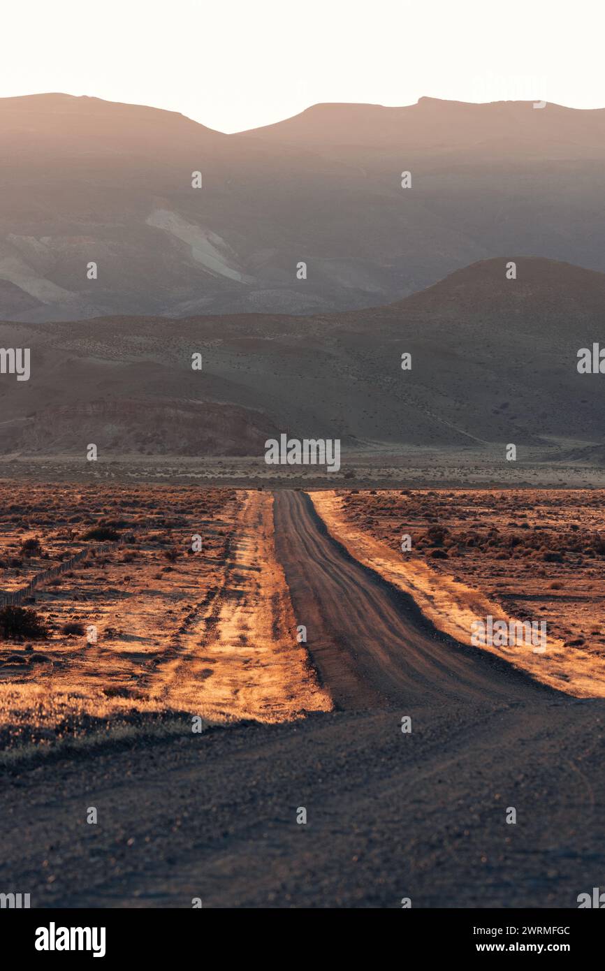 Die untergehende Sonne wirft ein warmes Leuchten über eine gewundene Feldstraße durch die patagonische Wüste und lädt zu Abenteuern am ruhigen Abend ein Stockfoto