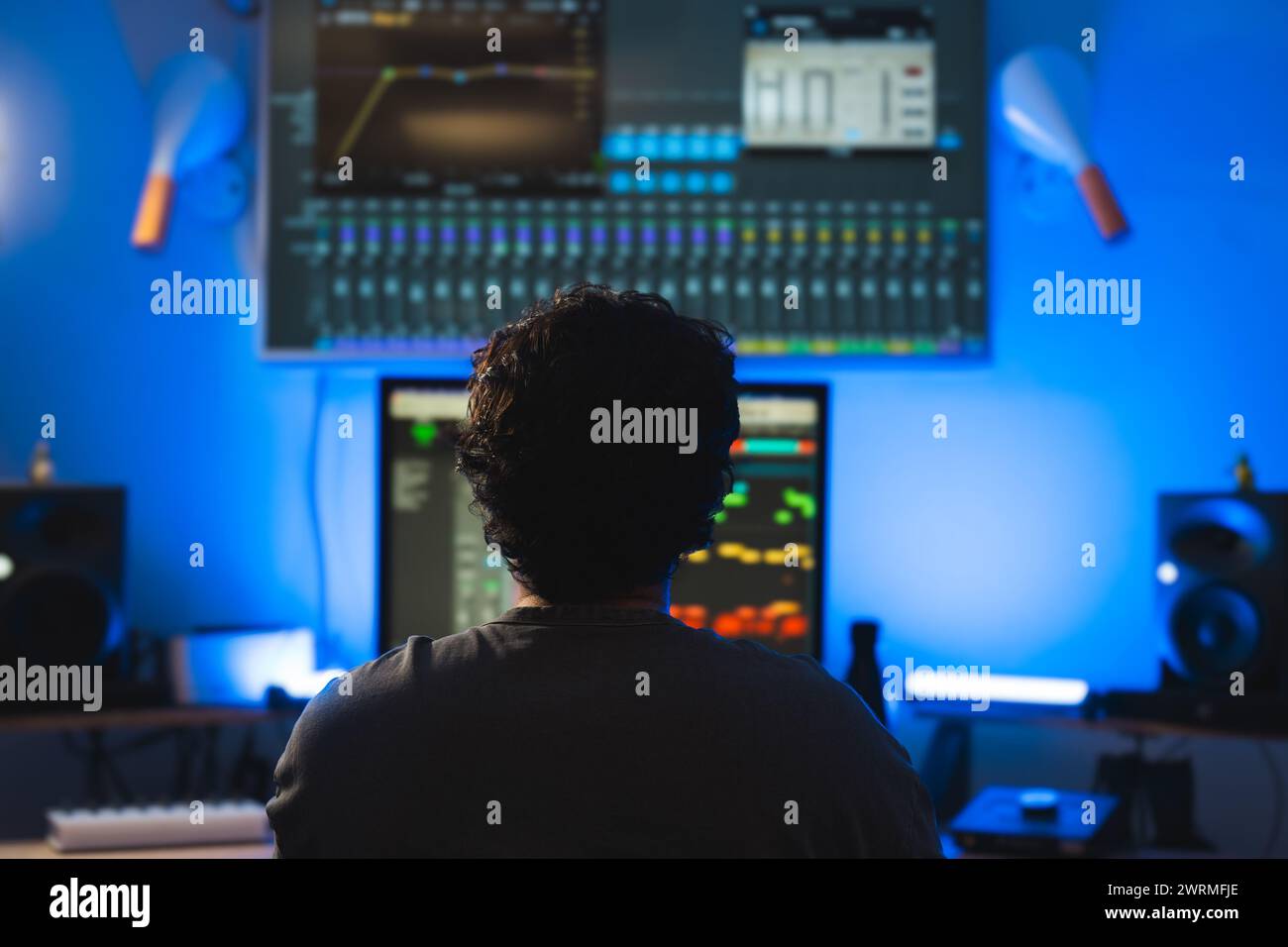 Während einer Aufnahme in einem Tonstudio mit blauem Umgebungslicht wird ein Produzent mit leuchtenden Bildschirmen und Audiogeräten in der Silhouette gehalten. Stockfoto